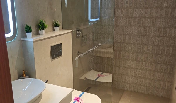 Modern bathroom interior in a 3 BHK apartment at Prestige Evergreen featuring a sleek white washbasin, LED-lit mirror, glass shower partition, and patterned wall tiles