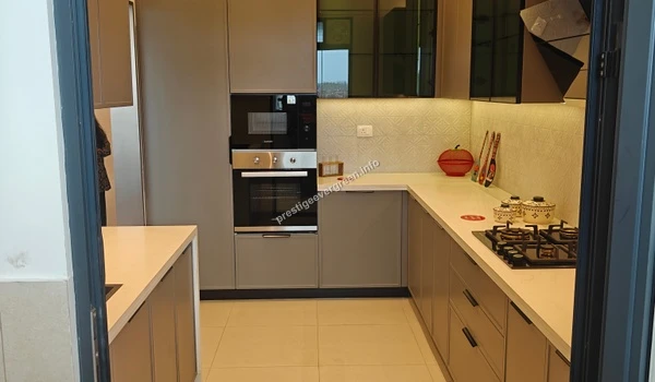 Complete overview of the modern L-shaped modular kitchen in a 3 BHK unit at Prestige Evergreen featuring grey cabinetry, white countertops, and high-end built-in appliances