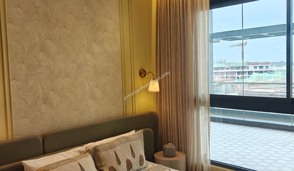 Elegant bedroom interior at Prestige Evergreen showcasing a leaf-patterned wallpaper, bedside lamp lighting, and large windows with curtains