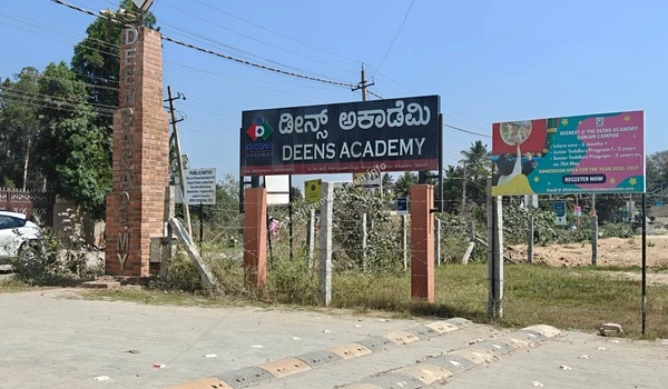 A wide view of the Deens Academy campus entry including the brick pillar and informational boards near the Prestige Evergreen site