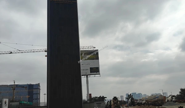 A towering black granite entrance pylon for Evergreen at Prestige Raintree Park located in Whitefield, Bengaluru, standing prominently against a cloudy sky next to a construction site with a large crane.