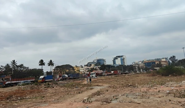 A perspective view of the wide internal road at the Prestige Evergreen site, flanked by large advertising billboards and construction cranes under an overcast sky.