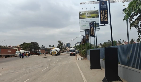 External boundary of the Prestige Evergreen construction site displaying prominent promotional billboards and banners, with high-rise cranes visible in the background against the skyline.
