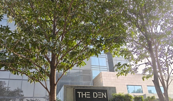 The Den hotel facade visible through lush greenery, representing the high-end hospitality neighbors of the Prestige Evergreen project