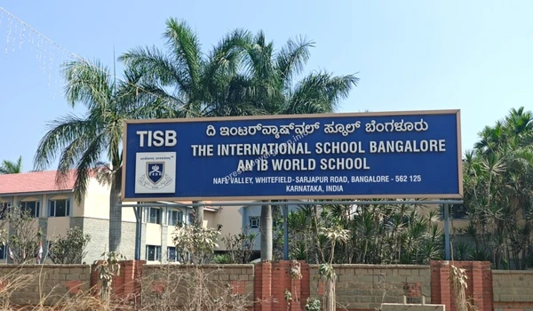 A clear view of the TISB (The International School Bangalore) signage with palm trees in the background near Prestige Evergreen